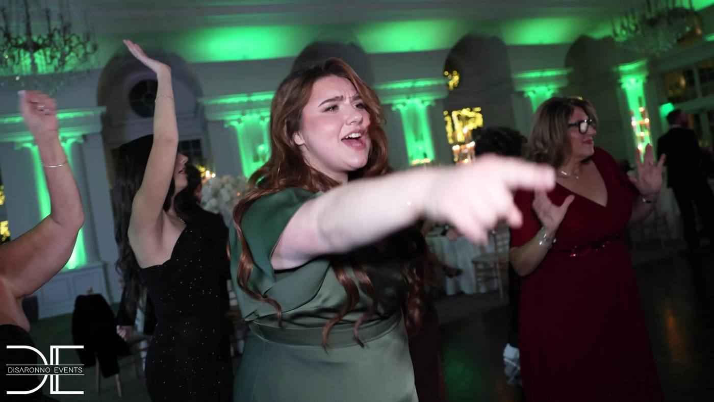 Guest singing along and pointing on the dance floor under green uplighting at a ballroom wedding
